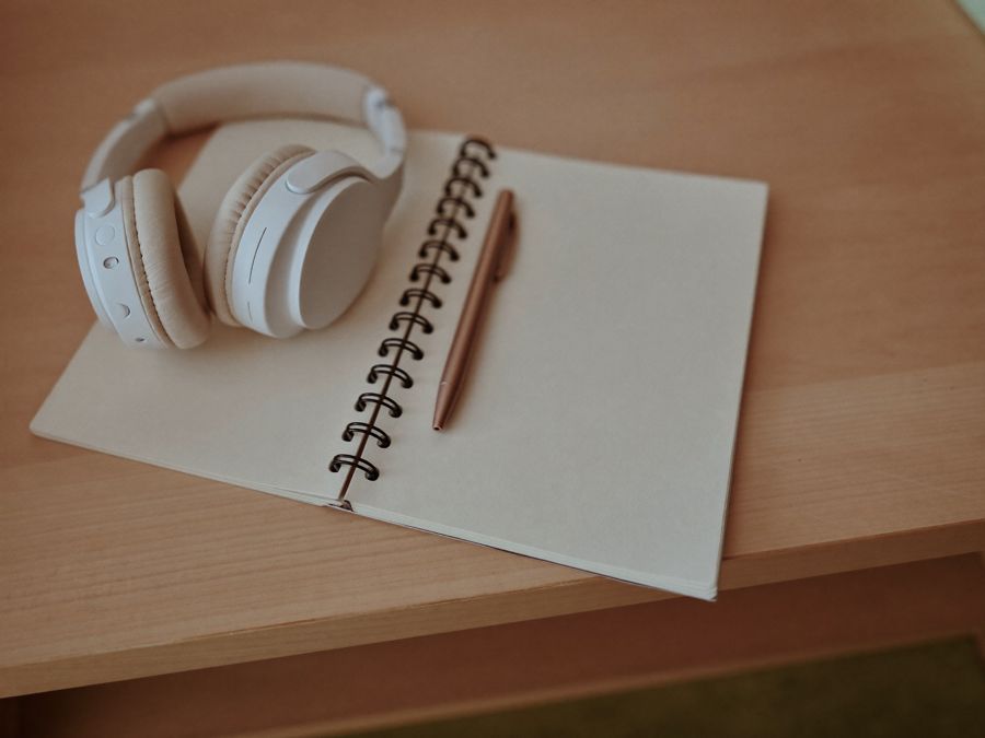 Caderno aberto com caneta e fone de ouvido sobre uma mesa