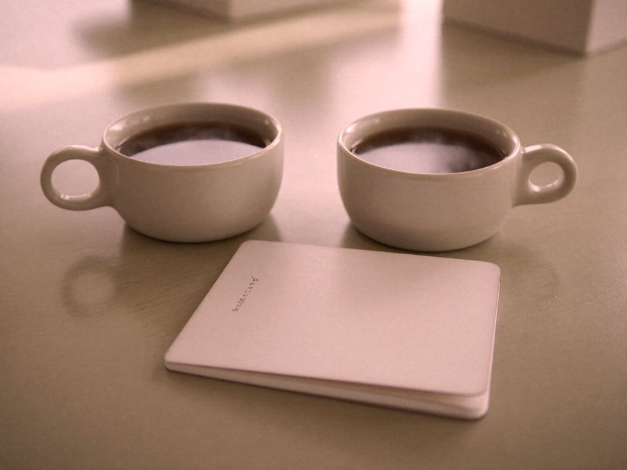 Duas xícaras sobre uma mesa clara, ao lado de um caderno